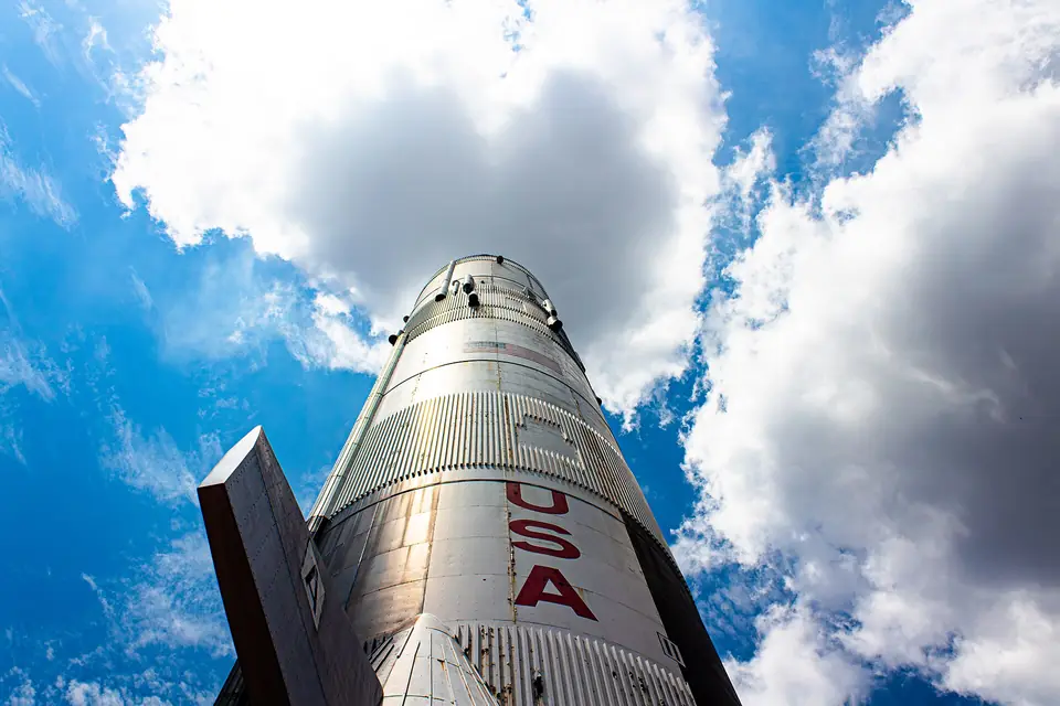 The full-size Saturn V rocket replica at the U.S. Space & Rocket Center in Huntsville, seen from below against a bright blue sky and white clouds
